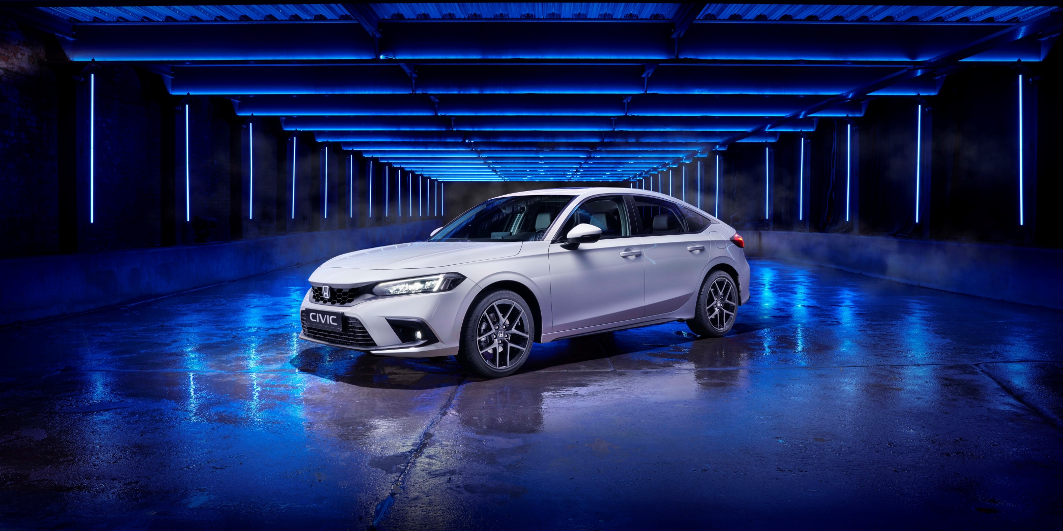 En ny 2022 Honda Civic, set skråt forfra, med hvid finish og fotograferet i studie med blå belysning